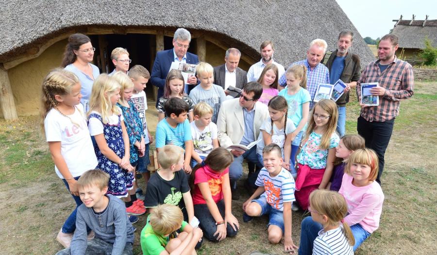 Die 4. Klasse der Hilteraner Grundschule Wellendorf bekam von Autor Frank Huismann (sitzend) eine Leseprobe über das Eisenzeithaus in Ostercappeln-Venne aus der neuen Ausgabe des Unterrichts- und Leseheftes „Museen – Muss ich sehen! Neues von Jutta und Benno im Osnabrücker Land“. Mitglieder des Redaktionsteams verteilten zusammen mit Kreisrat Matthias Selle (hintere Reihe, 3 v. l.) und Burkhard Fromme (hintere Reihe, 3 v. r), Leiter des Kulturbüros beim Landkreis, anschließend die Hefte an die Kinder. 