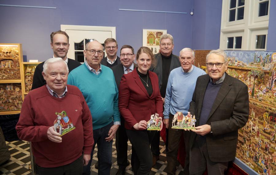 Der Künstler Josef Morgret (links) hat in jahrelanger Arbeit eine riesige Papierkrippe geschaffen, die nun im Museum im Kloster zu sehen ist. Figuren daraus präsentieren neben Morgret (von links)  Pfarrer Jan Witte, Manfred Kalmlage (Heimatverein Bersenbrück), Bürgermeister Michael Wernke (Samtgemeinde Bersenbrück), Jürgen Krämer (Krippenverein), Katharina Pfaff (Museum im Kloster/Kulturbüro), Kreisrat Matthias Selle, Franz Buitmann (Heimatverein Bersenbrück) sowie Gerhard Lohmeier (Krippenverein). Foto: La