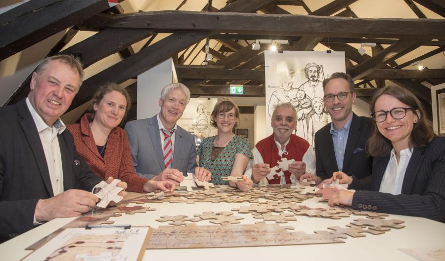 Das großformatige Puzzle des Friedensvertrages in der Ausstellung „Lebensbilder“ präsentieren (von links) der stellvertretende Landrat Werner Lager, Katharina Pfaff (Kulturbüro des Landkreises Osnabrück), Thomas Brakmann, Anna Philine Schöpper (beide Niedersächsisches Landesarchiv, Abteilung Osnabrück), Liedermacher Günter Gall, Pfarrer Jan Wilhelm Witte und Judith Franzen (Stadt- und Kreisarchäologie Osnabrück). Foto: Uwe Lewandowski