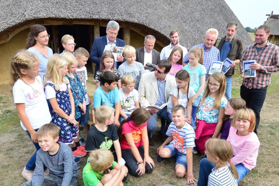 Die 4. Klasse der Hilteraner Grundschule Wellendorf bekam von Autor Frank Huismann (sitzend) eine Leseprobe über das Eisenzeithaus in Ostercappeln-Venne aus der neuen Ausgabe des Unterrichts- und Leseheftes „Museen – Muss ich sehen! Neues von Jutta und Benno im Osnabrücker Land“. Mitglieder des Redaktionsteams verteilten zusammen mit Kreisrat Matthias Selle (hintere Reihe, 3 v. l.) und Burkhard Fromme (hintere Reihe, 3 v. r), Leiter des Kulturbüros beim Landkreis, anschließend die Hefte an die Kinder. 