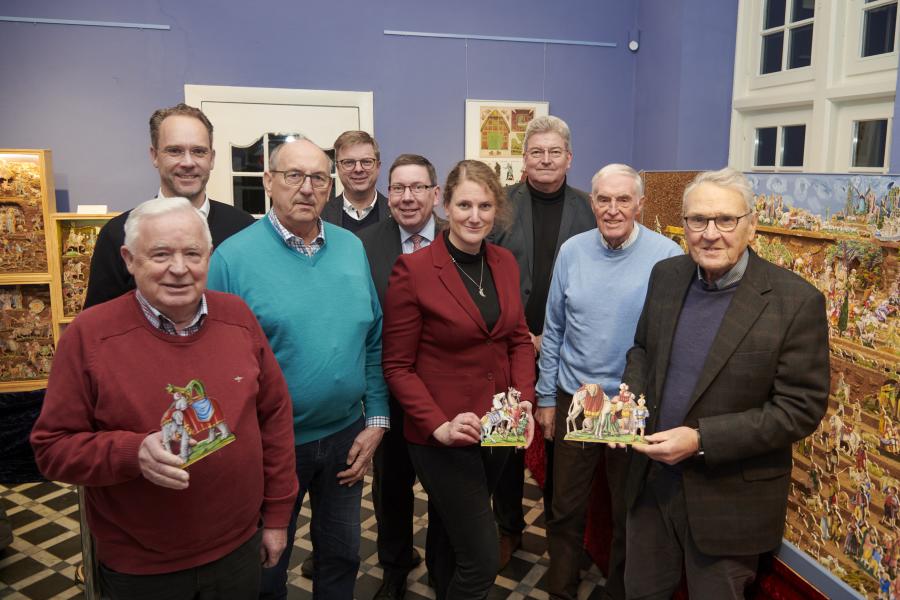 Der Künstler Josef Morgret (links) hat in jahrelanger Arbeit eine riesige Papierkrippe geschaffen, die nun im Museum im Kloster zu sehen ist. Figuren daraus präsentieren neben Morgret (von links)  Pfarrer Jan Witte, Manfred Kalmlage (Heimatverein Bersenbrück), Bürgermeister Michael Wernke (Samtgemeinde Bersenbrück), Jürgen Krämer (Krippenverein), Katharina Pfaff (Museum im Kloster/Kulturbüro), Kreisrat Matthias Selle, Franz Buitmann (Heimatverein Bersenbrück) sowie Gerhard Lohmeier (Krippenverein). Foto: La