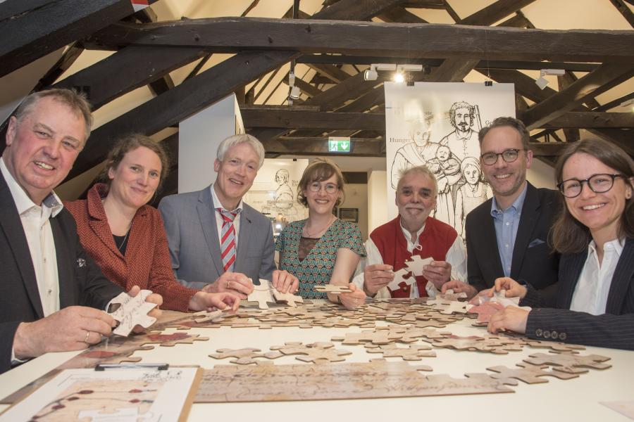 Das großformatige Puzzle des Friedensvertrages in der Ausstellung „Lebensbilder“ präsentieren (von links) der stellvertretende Landrat Werner Lager, Katharina Pfaff (Kulturbüro des Landkreises Osnabrück), Thomas Brakmann, Anna Philine Schöpper (beide Niedersächsisches Landesarchiv, Abteilung Osnabrück), Liedermacher Günter Gall, Pfarrer Jan Wilhelm Witte und Judith Franzen (Stadt- und Kreisarchäologie Osnabrück). Foto: Uwe Lewandowski